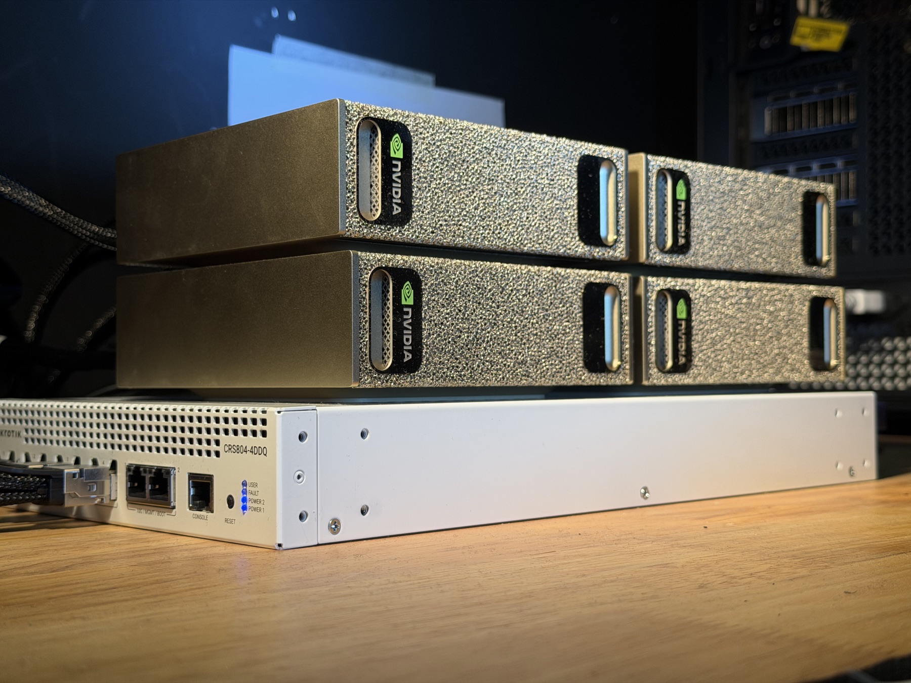 Four NVIDIA DGX Spark nodes stacked on a 100-gigabit switch on a wooden bench, cabled and running.